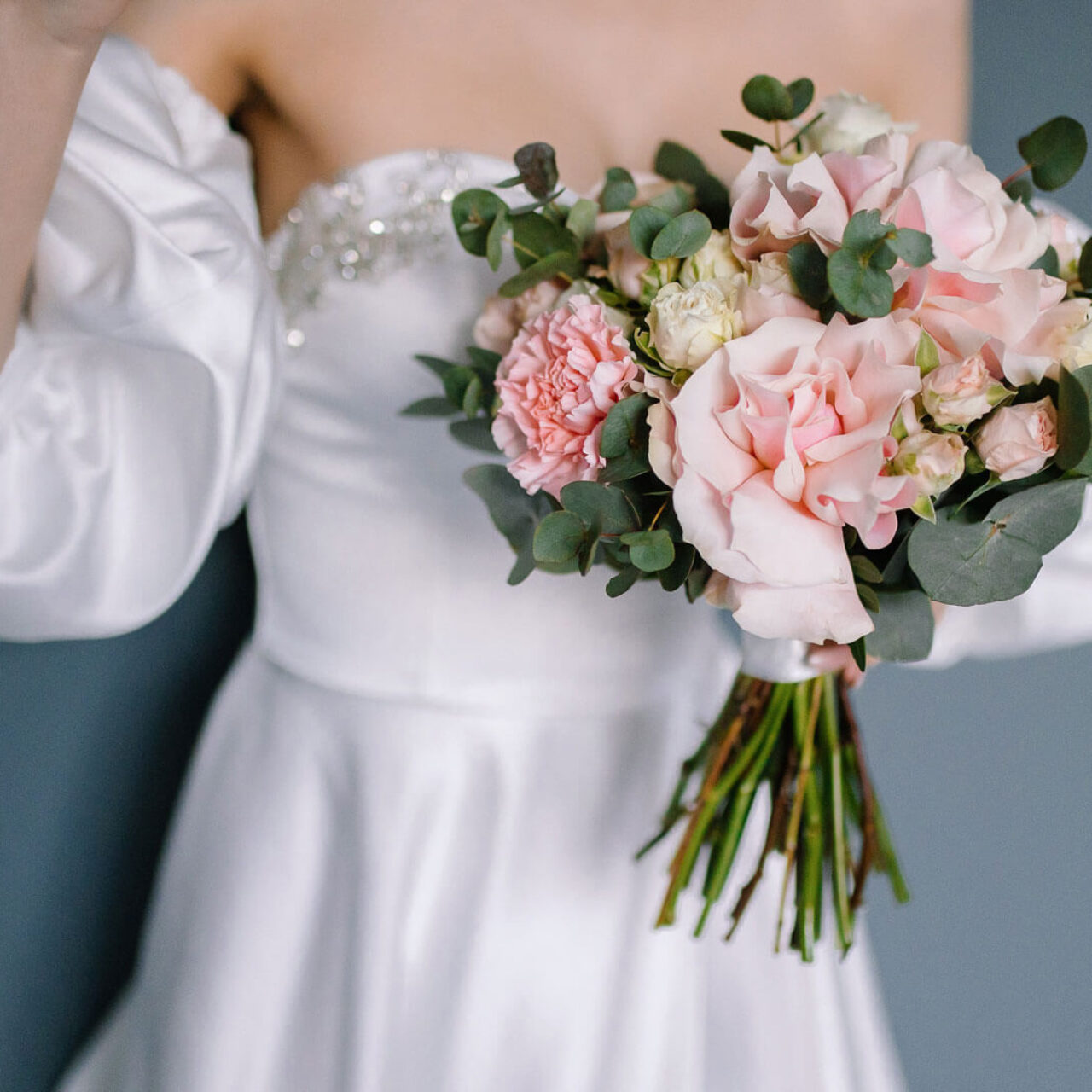 Braut in einem weißen Kleid hält einen Blumenstrauß mit rosa und weißen Blumen.