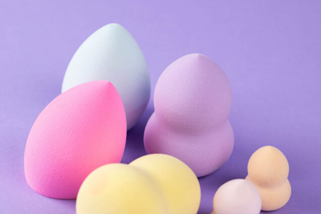 Bunte Make-up-Schwämmchen in verschiedenen Größen und Formen auf einem lila Hintergrund