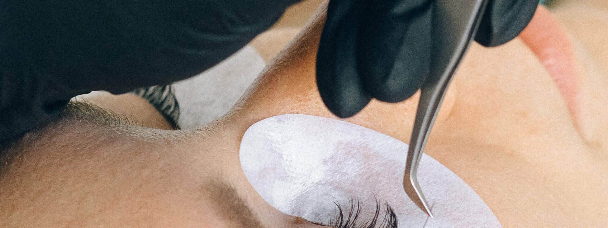 Close-up einer Wimpernverlängerung, bei der eine Kosmetikerin mit schwarzen Handschuhen einzelne Wimpern mit einer Pinzette aufträgt