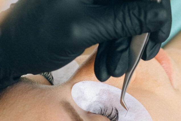 Close-up einer Wimpernverlängerung, bei der eine Kosmetikerin mit schwarzen Handschuhen einzelne Wimpern mit einer Pinzette aufträgt