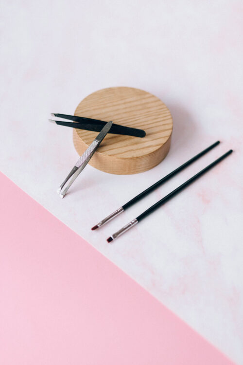 Makeup-Pinsel und Pinzetten, die auf einem runden Holzständer und einem rosa Hintergrund arrangiert sind.