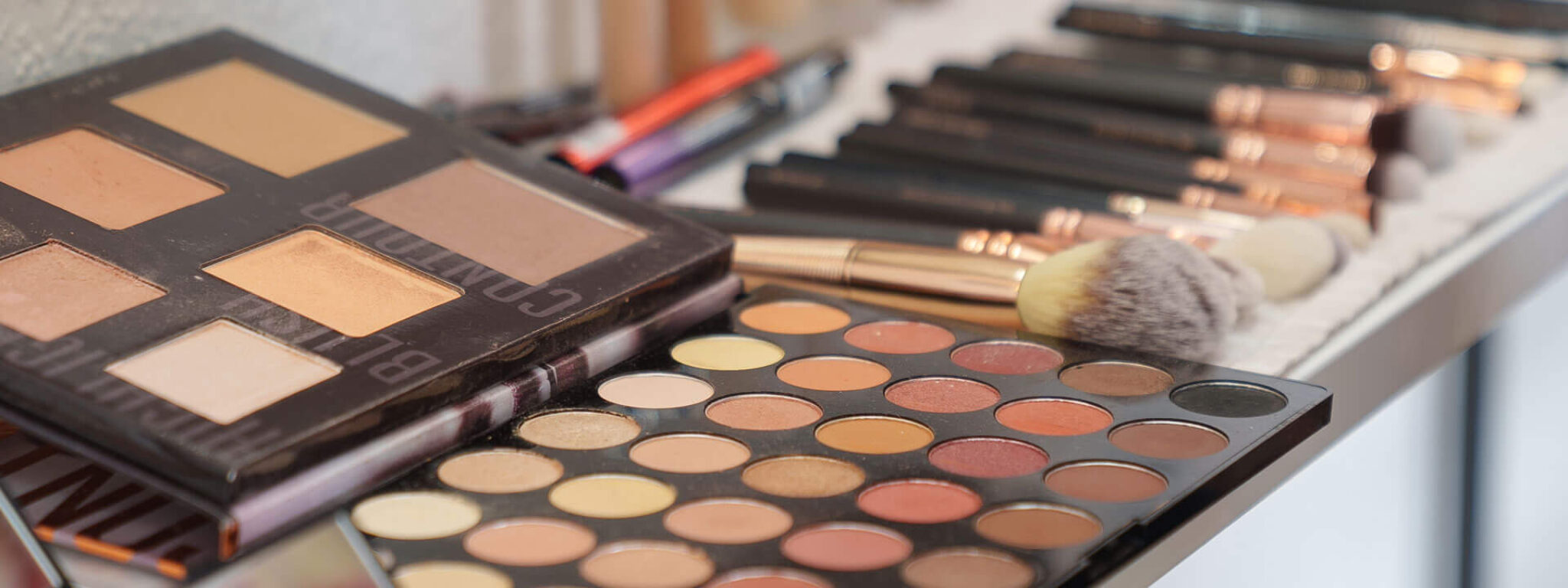 Verschiedene Make-up-Paletten und Kosmetikprodukte auf einem Schminktisch für eine Beauty-Beratung.