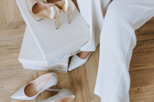 Elegante Schuhe und eine Einkaufstasche neben einer Person in weißer Hose.