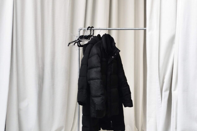 Kleiderständer mit schwarzer Jacke, vor einem Hintergrund aus beigen Vorhängen in einem minimalistischen Studio-Setup.