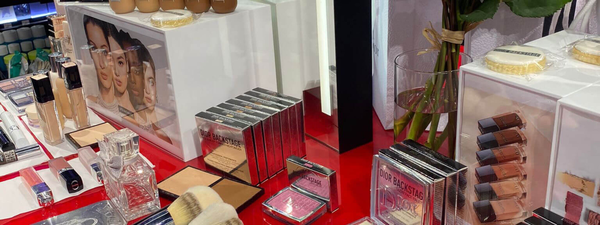 Make-up-Display mit verschiedenen Produkten wie Pinseln, Paletten und Foundations, dekoriert mit Blumen, in einem Kosmetikgeschäft.