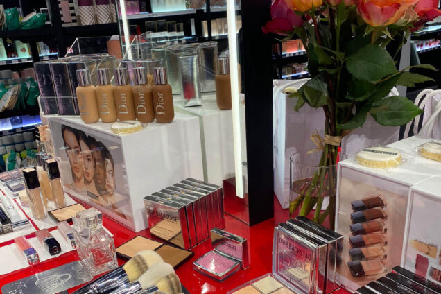 Make-up-Display mit verschiedenen Produkten wie Pinseln, Paletten und Foundations, dekoriert mit Blumen, in einem Kosmetikgeschäft.