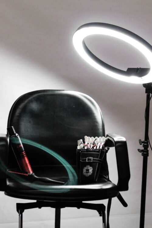 Ein Friseurstuhl mit Friseurutensilien und einem großen Ringlicht im Hintergrund, bereit für eine Beauty- oder Friseur-Session.