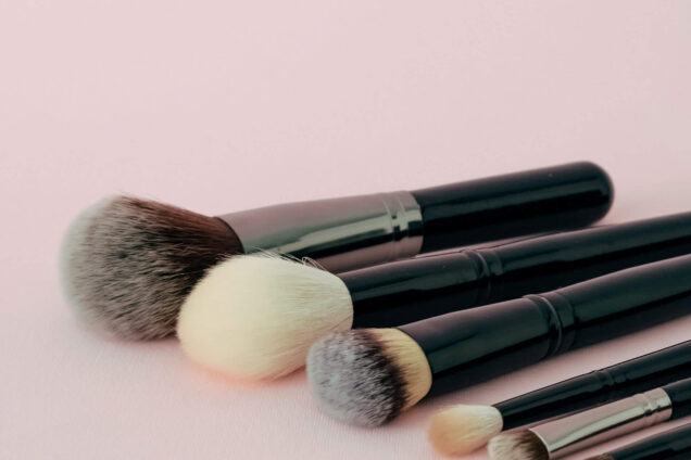 Eine Auswahl an Make-up-Pinseln auf einem rosa Hintergrund arrangiert.