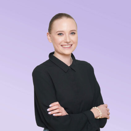 Porträt einer lächelnden Frau mit zurückgebundenen Haaren in einem schwarzen Oberteil vor einem hellvioletten Hintergrund.