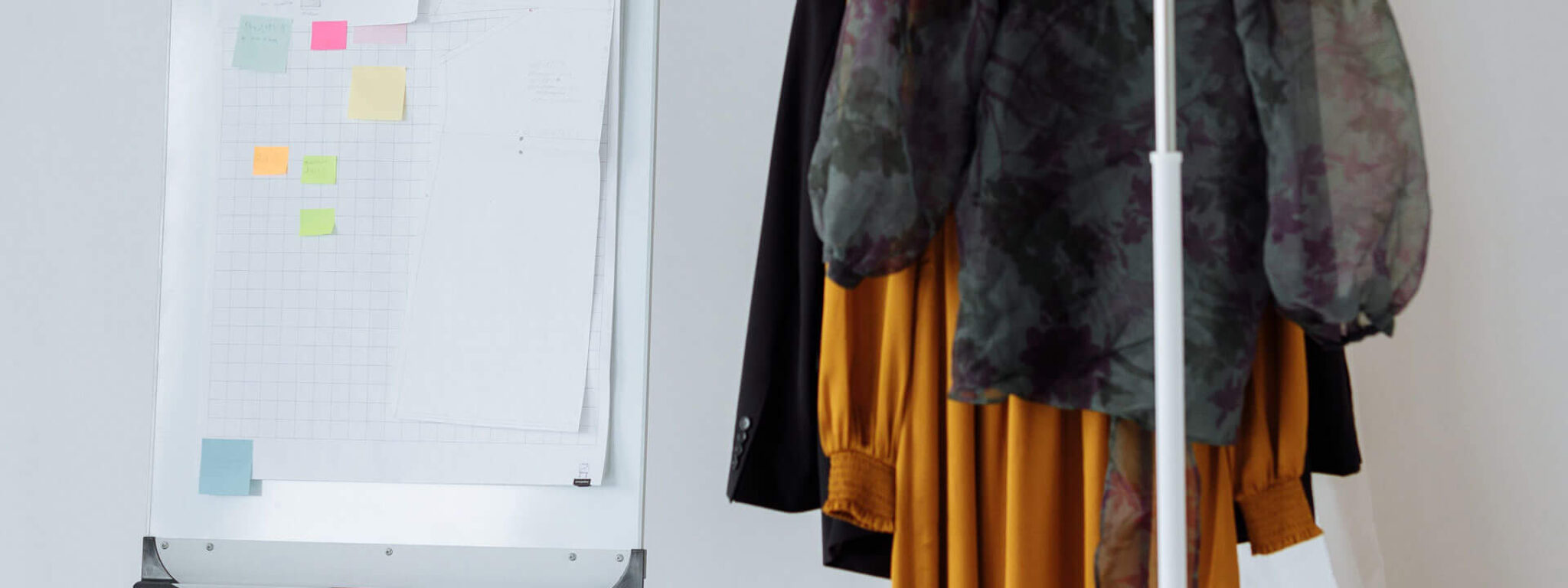 Kleiderständer mit gelbem Kleid und Flipchart mit Notizen in einem hellen Raum